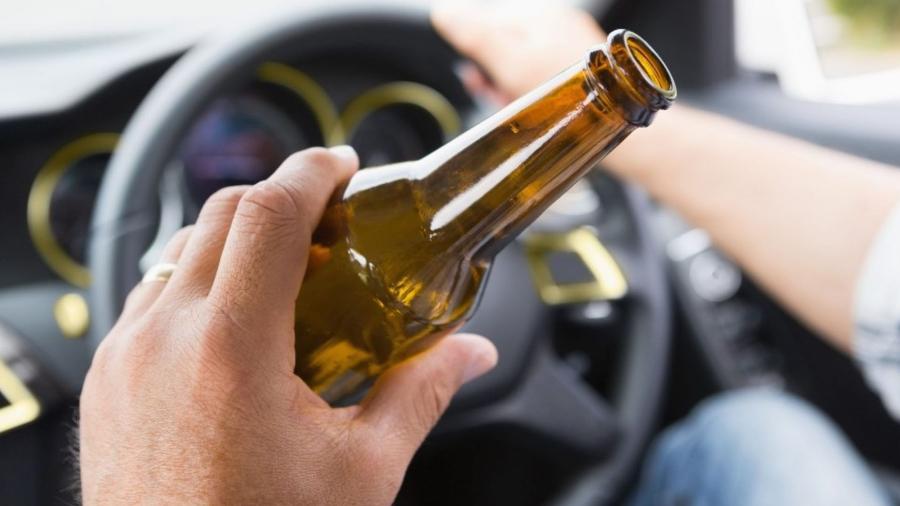 Mão masculina segurando garrafa de cerveja no volante de carro em movimento
