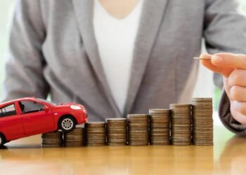 Pessoa empilhando moedas ao lado de carro vermelho de brinquedo sobre mesa de madeira