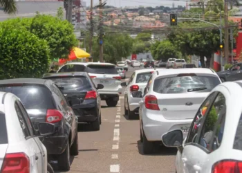 Diversos carros parados em fila dupla em avenida movimentada sob luz do dia