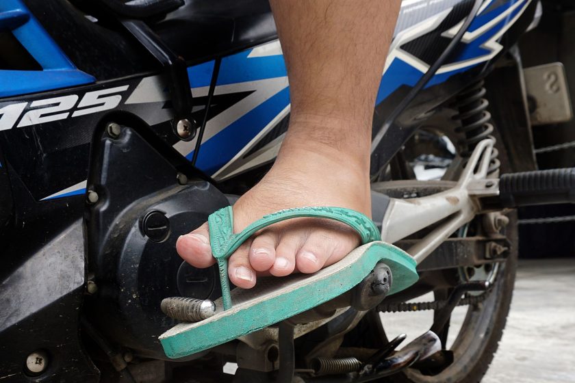 Pé calçando chinelo verde apoiado no pedal de moto azul e preta