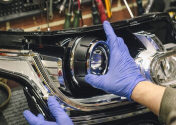 Mãos com luvas azuis ajustando farol de LED em lanterna automotiva