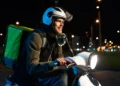 Motociclista com mochila de entrega dirige scooter à noite em avenida iluminada