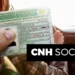 Pessoa segura CNH enquanto dirige carro, destaque para documento