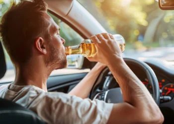 Homem dirigindo carro enquanto bebe cerveja em garrafa de vidro com painel ao fundo