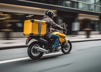 Motociclista com mochila amarela realiza entrega em avenida movimentada de São Paulo