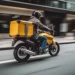 Motociclista com mochila amarela realiza entrega em avenida movimentada de São Paulo