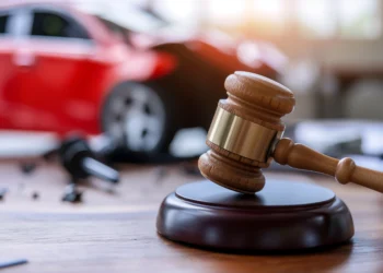 Martelo de juiz sobre mesa de madeira com carro vermelho acidentado ao fundo