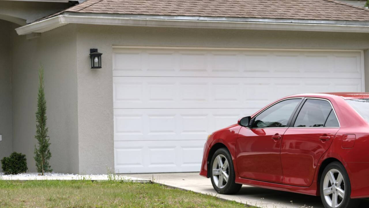 Veículo vermelho parado em frente ao portão branco de garagem residencial