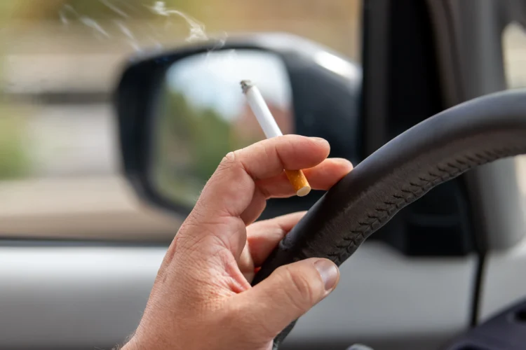 Condutor dirige veículo segurando cigarro aceso com mão no volante