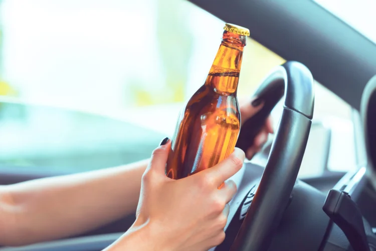 Mãos femininas segurando volante e garrafa de bebida em carro com luz natural