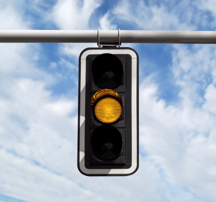 Sinal de trânsito aceso no amarelo sob céu azul com nuvens