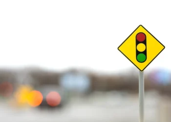 Placa amarela com desenho de semáforo em destaque à frente de trânsito desfocado