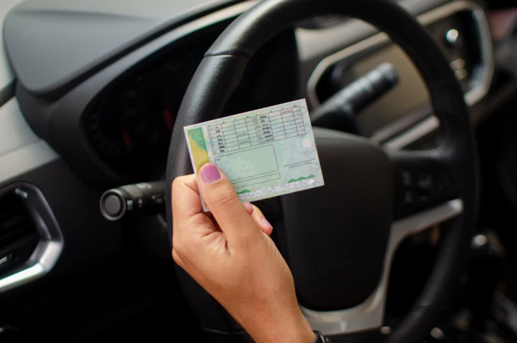 Pessoa segurando CNH renovada próximo ao volante do veículo