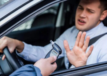 Homem no carro faz gesto de recusa enquanto policial oferece bafômetro pela janela