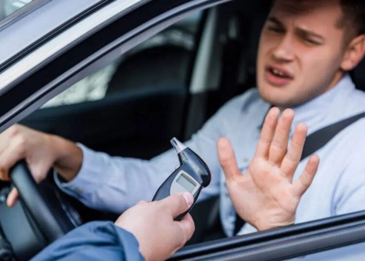 Homem no carro faz gesto de recusa enquanto policial oferece bafômetro pela janela