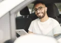 Homem sorridente dentro de carro segura tablet enquanto aguarda renovação digital da CNH