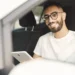 Homem sorridente dentro de carro segura tablet enquanto aguarda renovação digital da CNH