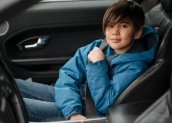 Criança de casaco azul usando cinto de segurança no banco da frente do carro