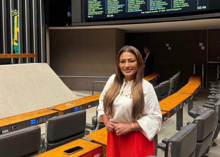 Mulher de cabelos longos e castanhos veste blusa branca e saia vermelha em plenário da Câmara dos Deputados