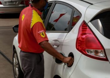 Frentista com camisa vermelha e amarela da Shell abastece Ford Fiesta branco em posto de combustíveis
