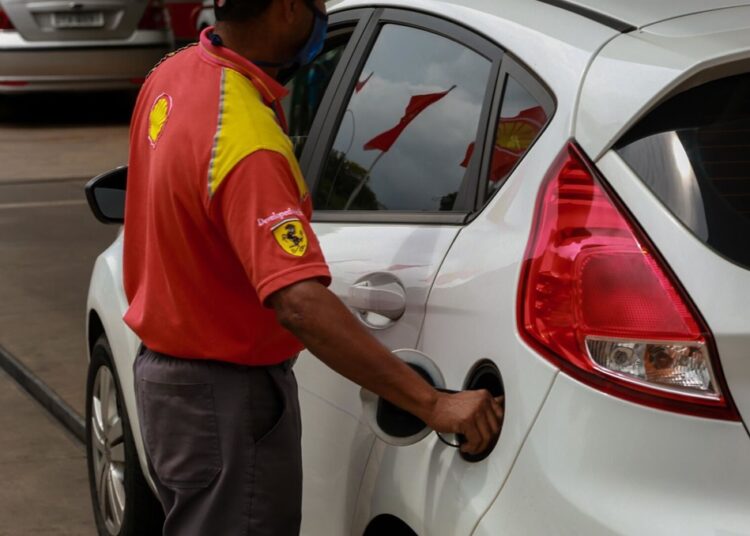 Frentista com camisa vermelha e amarela da Shell abastece Ford Fiesta branco em posto de combustíveis