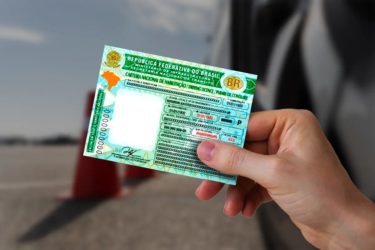 Mão segurando Carteira Nacional de Habilitação brasileira com mapa do Brasil, emblema da República e fundo com cones de trânsito