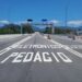 Rodovia com inscrição "PEDÁGIO ELETRÔNICO" no asfalto, pórtico metálico com câmeras e montanhas ao fundo