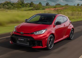 Toyota GR Yaris vermelho com detalhes em preto trafega por estrada asfaltada com paisagem verde ao fundo
