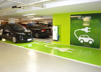 Dois carros elétricos conectados a carregador EVlink em vagas verdes com sinalização para veículos elétricos