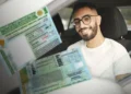 Homem de óculos, barba e camiseta branca exibe duas CNHs brasileiras dentro de um veículo