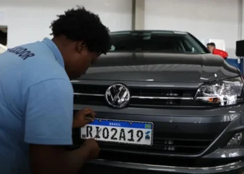 Funcionário uniformizado fixando placa padrão Mercosul RK02A19 em Volkswagen Virtus cinza