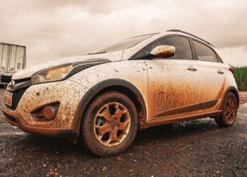 Hyundai HB20X branco estacionado totalmente coberto por barro vermelho após passagem por estrada de terra