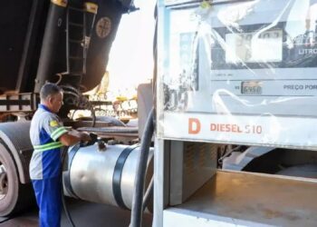 Homem abastecendo caminhão em posto de combustível; bomba exibe preço do diesel S10