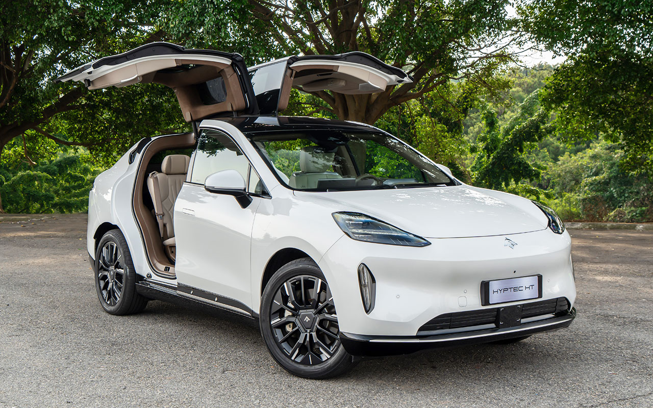 SUV elétrico branco Hyptec HT com portas traseiras asa de gaivota abertas, interior marrom, em área arborizada