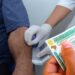 Profissional usando luvas coleta amostra de pelo do braço de homem segurando CNH para exame toxicológico