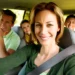 Mulher sorridente dirige carro com família ao fundo, usando cinto de segurança em dia ensolarado de viagem