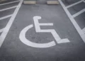 Vaga de estacionamento PCD com símbolo de cadeirante pintado em branco sobre asfalto cinza e faixas de demarcação.