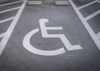 Vaga de estacionamento PCD com símbolo de cadeirante pintado em branco sobre asfalto cinza e faixas de demarcação.