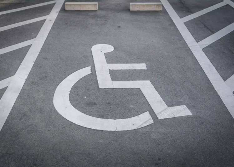 Vaga de estacionamento PCD com símbolo de cadeirante pintado em branco sobre asfalto cinza e faixas de demarcação.