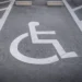 Vaga de estacionamento PCD com símbolo de cadeirante pintado em branco sobre asfalto cinza e faixas de demarcação.