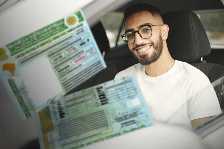 Homem jovem com óculos e barba sorri dentro de carro ao lado de duas CNHs brasileiras sobrepostas.