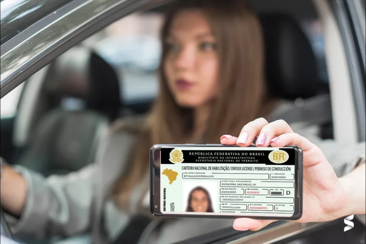 Mulher ao volante observa CNH digital exibida em smartphone por pessoa fora do veículo.