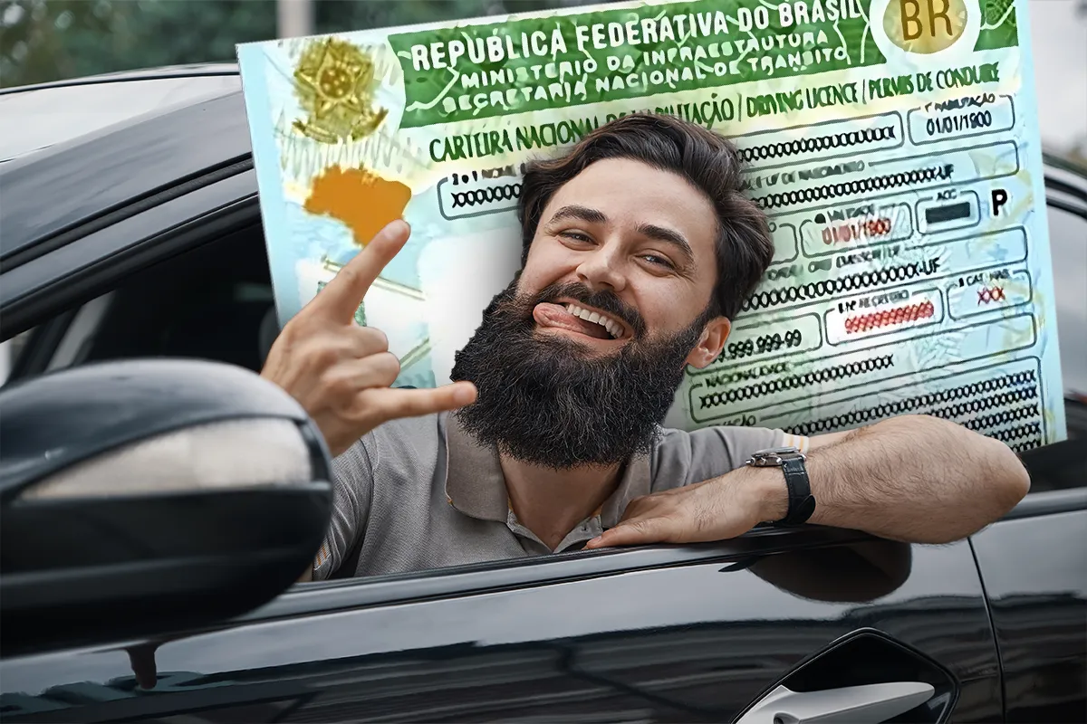Homem barbudo sorridente dentro de carro preto fazendo gesto de positivo com CNH do Brasil em segundo plano
