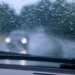 Visão do interior de um carro com gotas de chuva no para-brisa e faróis desfocados de veículo à frente
