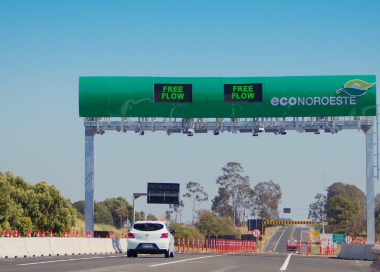 Carro branco passa sob pórtico verde Free Flow da EcoNoroeste em rodovia com sinalização de obras