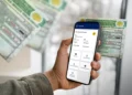 Mão segura smartphone com aplicativo CNH do Brasil mostrando dados do condutor, com CNH física brasileira desfocada ao fundo