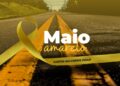 Laço amarelo sobre rodovia asfaltada com faixas contínuas e texto 'Maio Amarelo: Juntos Salvamos Vidas'.