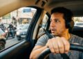 Homem de cabelos cacheados usando fone de ouvido enquanto dirige em trânsito intenso com motos e carros
