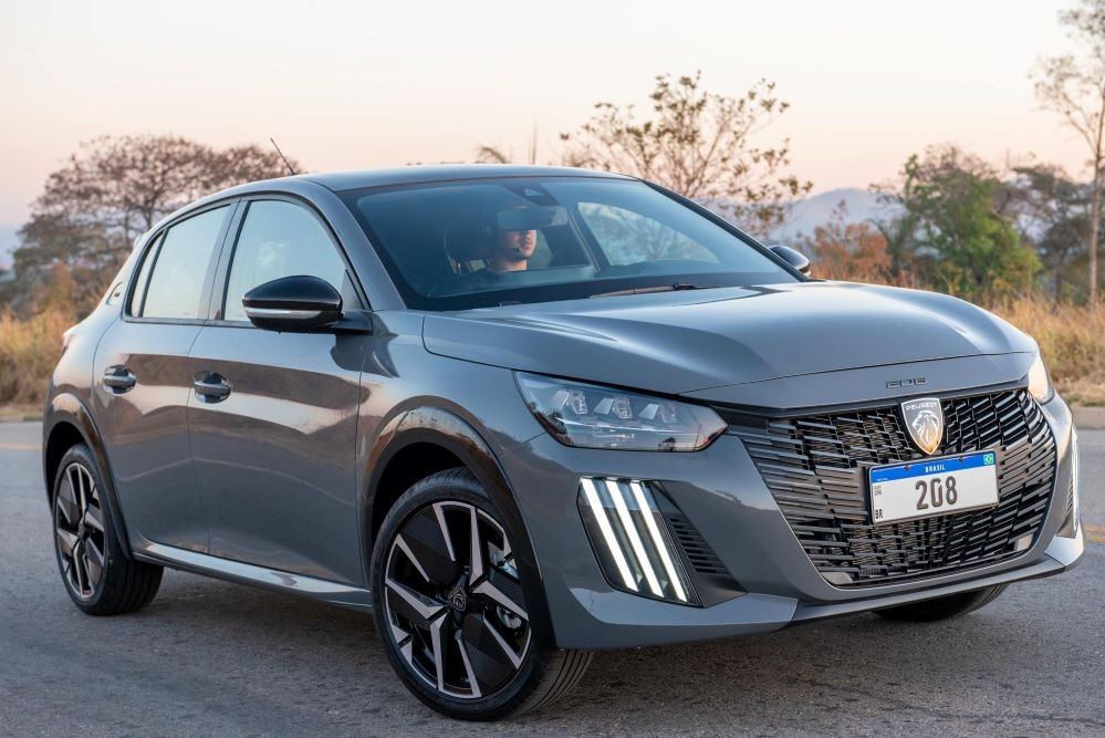 Peugeot 208 Allure cinza com placa 208, rodas diamantadas e faróis LED em cenário externo ao entardecer