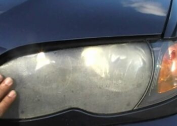 Mão apontando para farol de carro embaçado com lente opaca e sinais de umidade interna